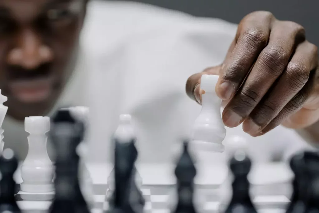A photograph showing an African-American man thinking and moving chess pieces on the board. 