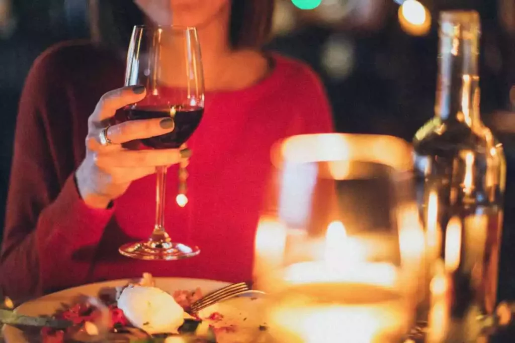 Young girlfriend having dinner in a candlelit restaurant with a glass of wine in her hand.