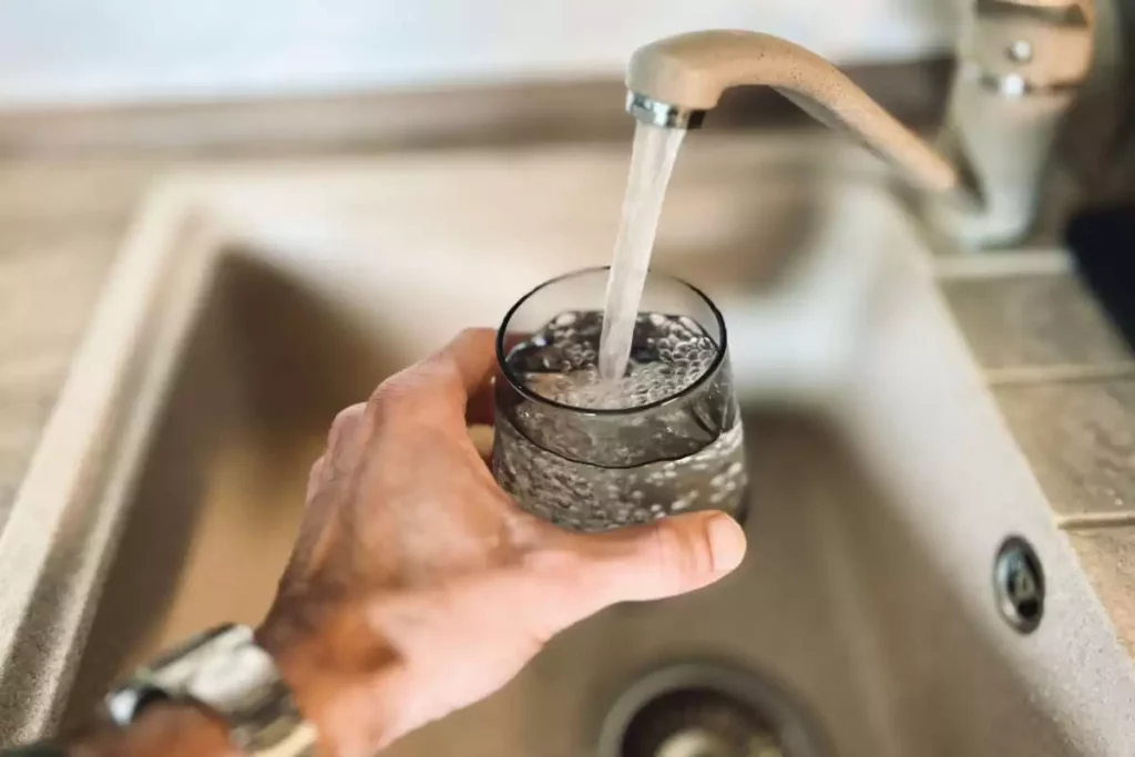 Man holding and filling a glass with drinking water under the sink tap.