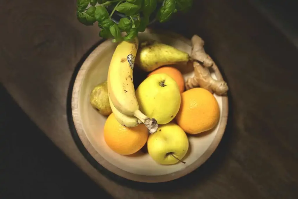 Healthy fruit like bananas, apples, oranges, ginger, pears and basil in a bowl on a wooden table.