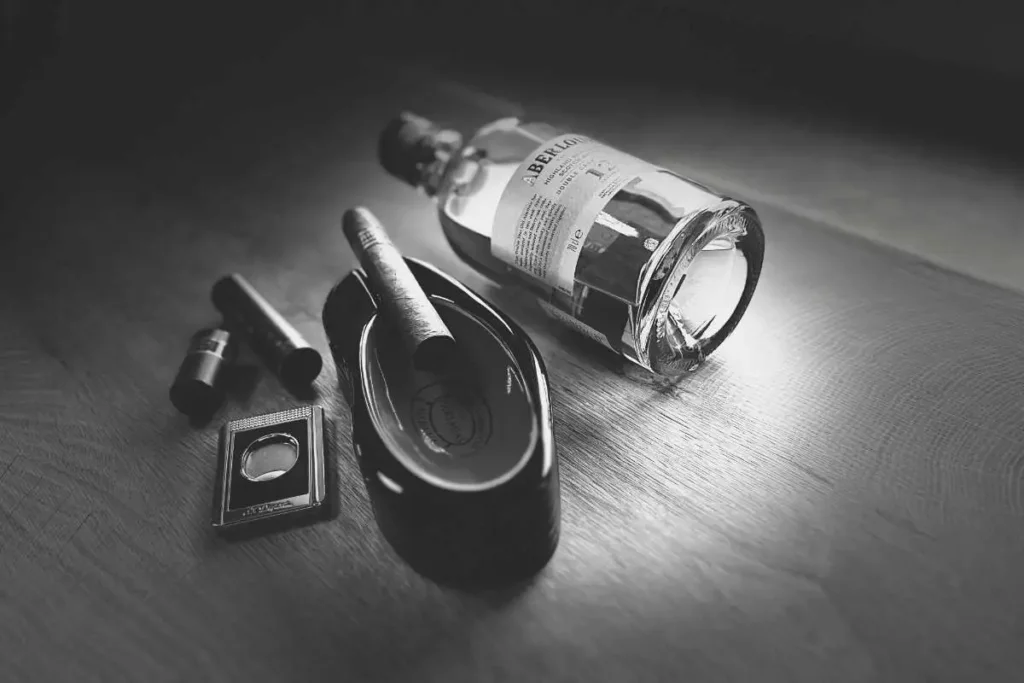 A black and white professional image of a Partagas Cuban cigar paired with Aberlour Whiskey, alongside Dupont cigar cutter.