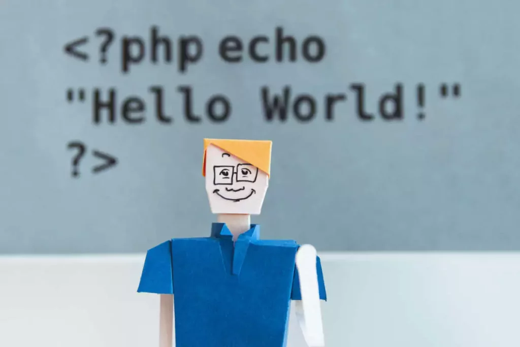 Photograph showing a character made out of paper and a title behind him showing code that says 'Hello World!'