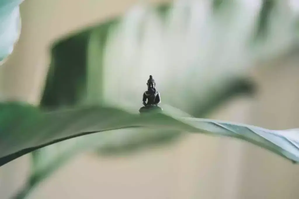 A small statue of Buddha sitting on a leaf in meditation pose. 