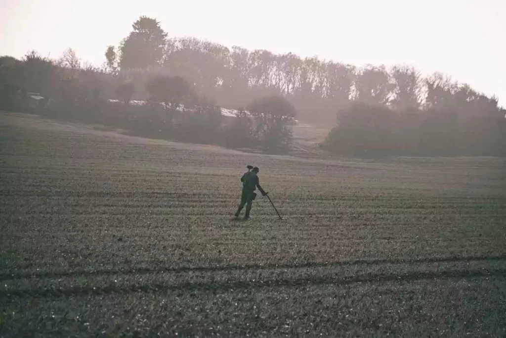 Hobbyist equipped with metal detector detecting in a large field.