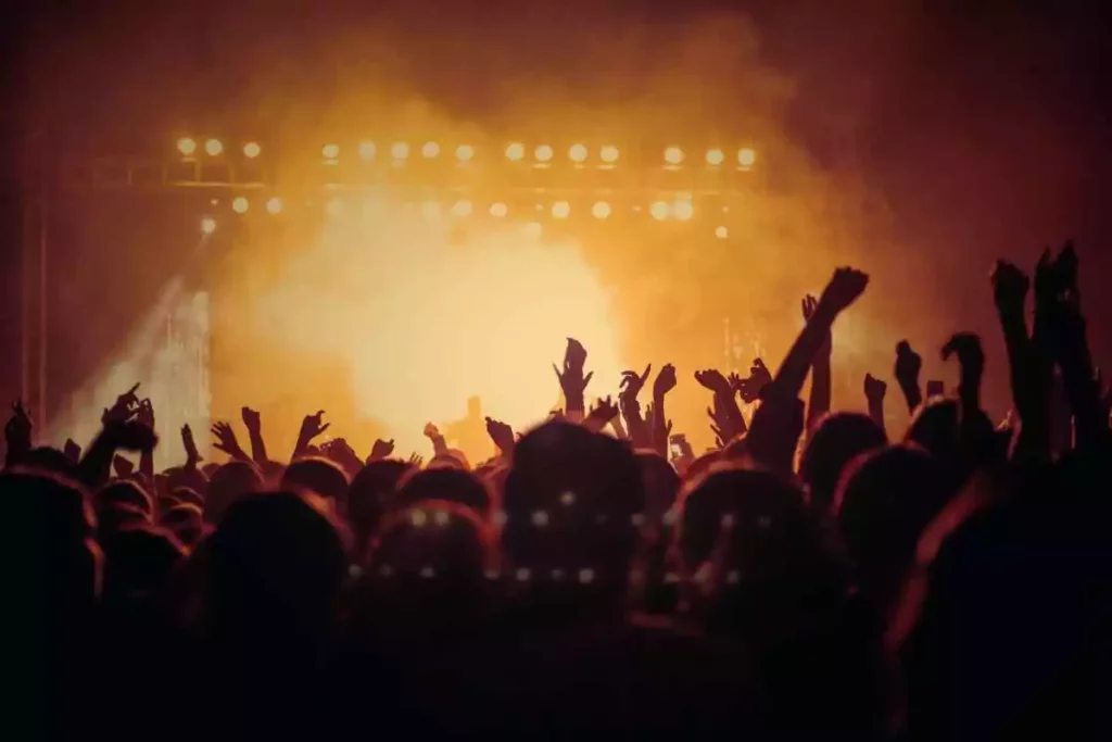 Crowd raising hands in a dimmed and smokey atmosphere at a night concert.