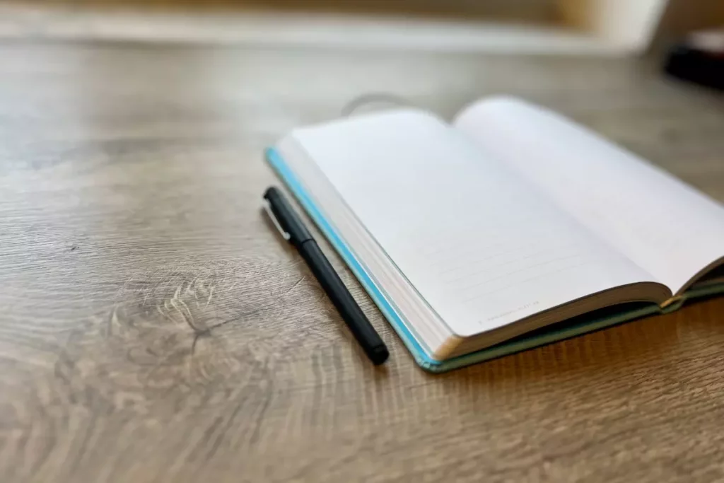 An open notebook and a pen which represent the need for writers to practice and write as much as they can in order to improve their writing skills.