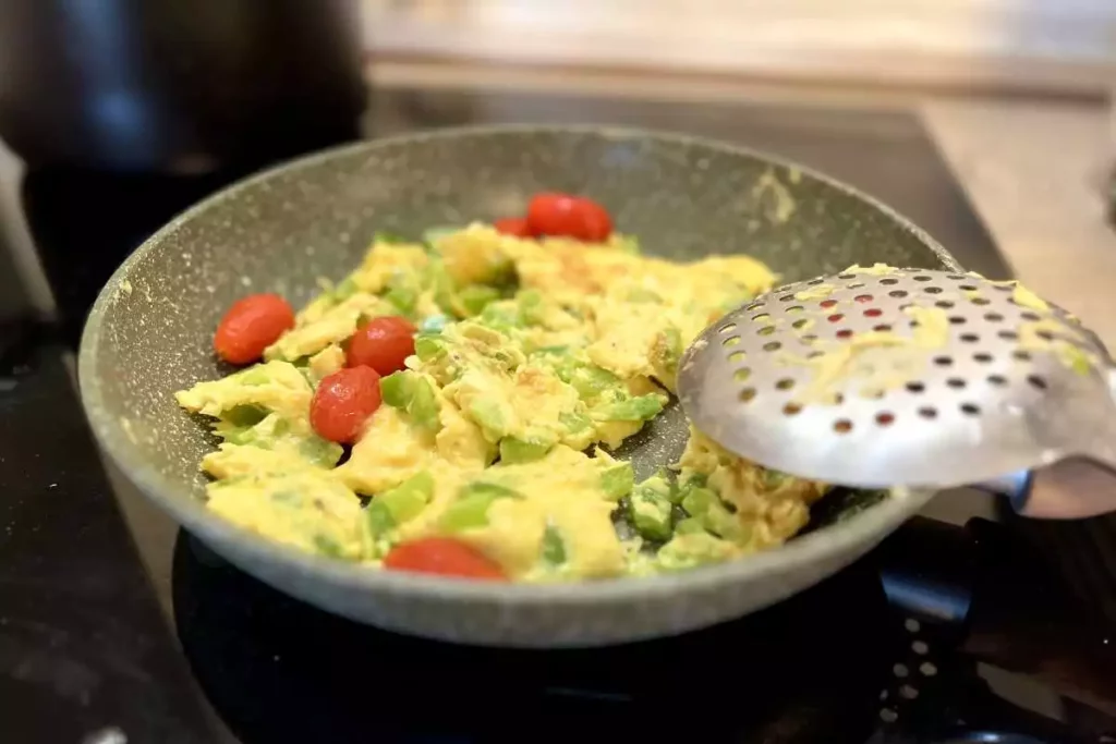 Making scrambled with eggs, tomatoes and asparagus as a fresh and healthy breakfast.