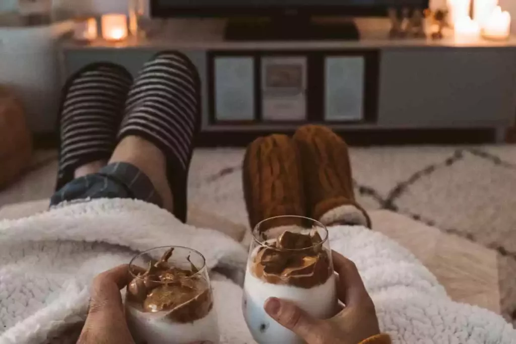 Boyfriend and girlfriend cuddling on couch while watching movie and drinking milkshakes.