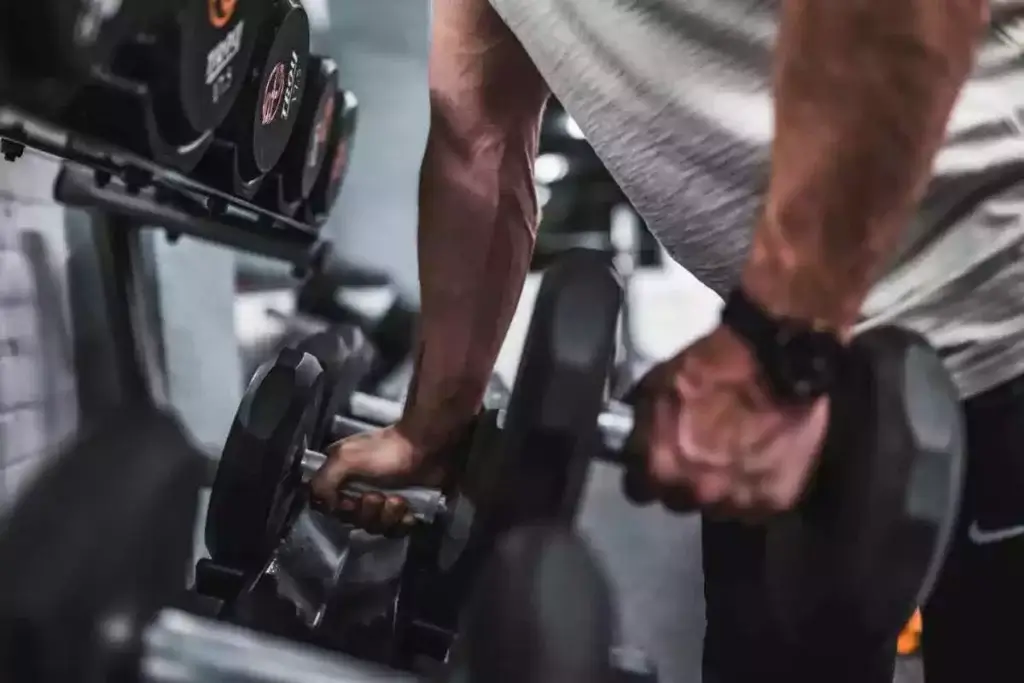 Well-built man wearing a sports watch working out and lifting weights in the gym.