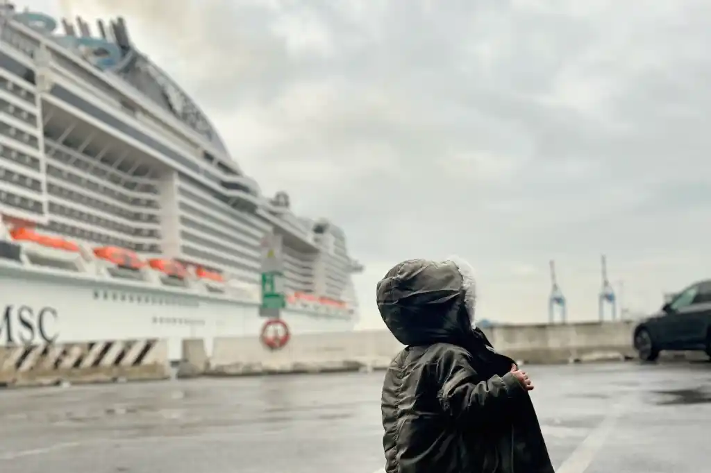 A baby girl pictured from behind standing next to a huge cruise ship MSC Bellissima in Port Genoa, Italy. 