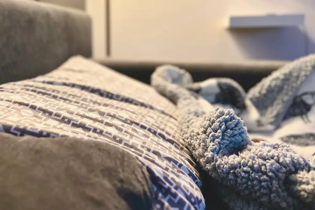 An image of a pillow and wool blanket on a bed, to show how good sleep is important for energy levels and production at work.