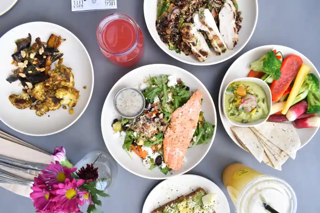 A photograph of a table filled with healthy muscle-building foods such as salmon, green vegetables, salads, broccoli, chicken,  peas, smoothies and more.