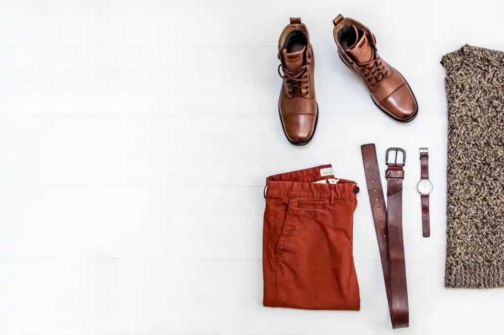 A photograph of stylish and fashionable clothes men can wear to impress their crush. Pictured are brown leather shoes, belt and wristwatch with red pants and a pullover.